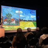 Jim Gilchrist presenting at the Interdisciplinary Research in the Arts Symposium, he is standing in front of a Vincent VanGough painting.